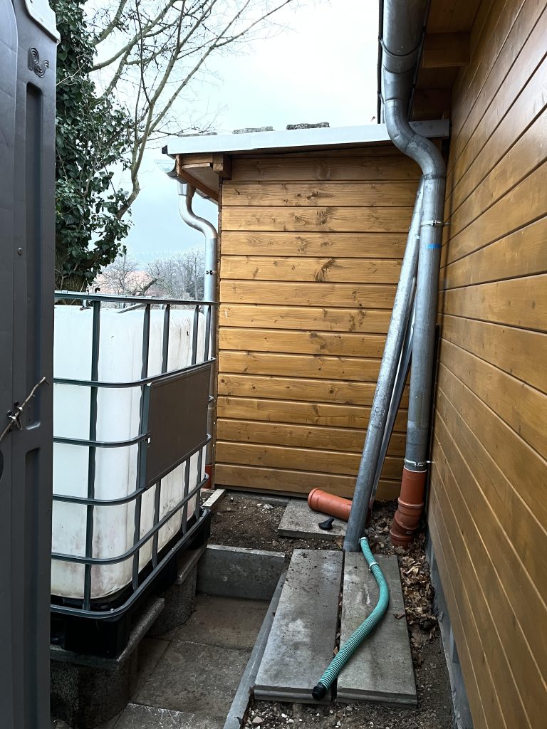 Ein 1000 Liter Fass wird als Regenwasserfass genutzt und wartet auf den Anschluss an die Dachrinne der Hütte