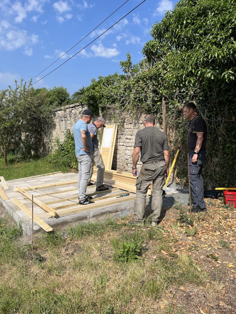 Vier Männer machen den Anfang und bauen das Gerätehaus auf der vorbereiteten Pflasterstein Fläche auf